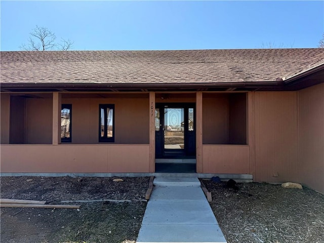 view of exterior entry with roof with shingles