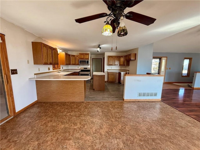 kitchen with open floor plan, a peninsula, appliances with stainless steel finishes, brown cabinetry, and baseboards