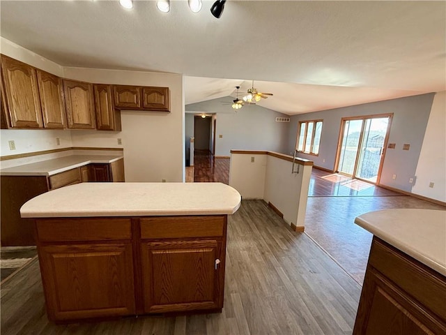 kitchen with wood finished floors, open floor plan, brown cabinetry, light countertops, and vaulted ceiling