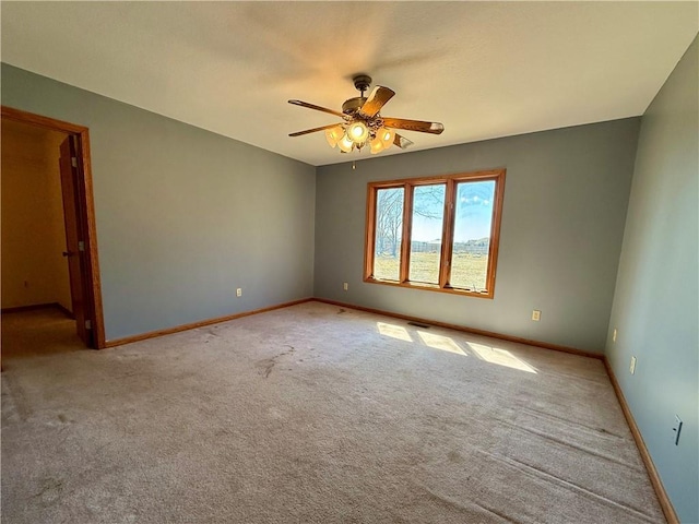 carpeted spare room featuring a ceiling fan and baseboards