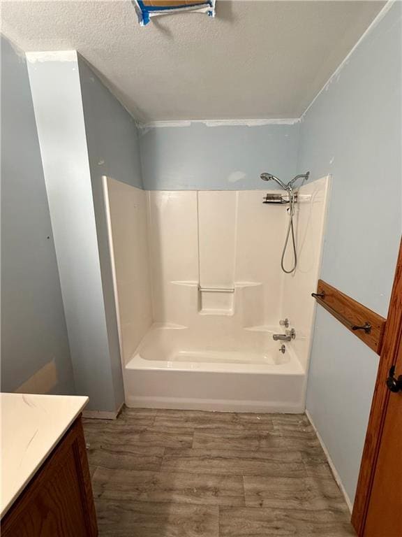 full bath featuring vanity, washtub / shower combination, wood finished floors, and a textured ceiling