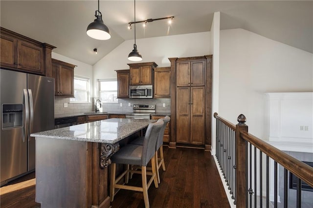 kitchen with a sink, light stone counters, a kitchen island, stainless steel appliances, and lofted ceiling