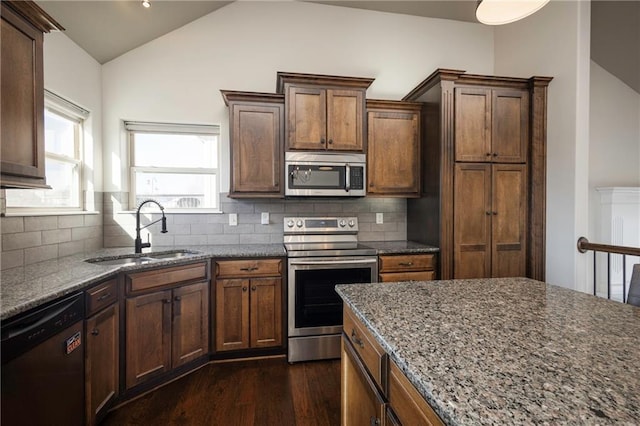 kitchen featuring dark wood finished floors, dark stone counters, a sink, stainless steel appliances, and vaulted ceiling