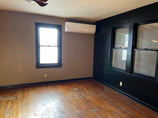 empty room with an AC wall unit, a ceiling fan, baseboards, and hardwood / wood-style floors