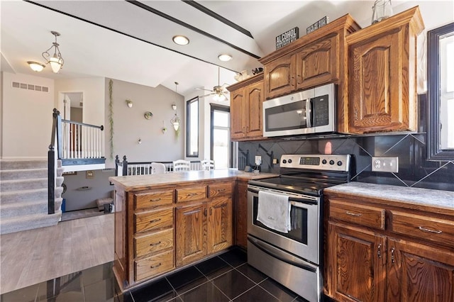 kitchen featuring visible vents, dark tile patterned flooring, backsplash, appliances with stainless steel finishes, and a peninsula