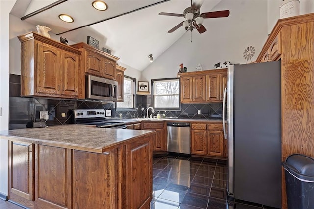 kitchen with brown cabinetry, a peninsula, a sink, decorative backsplash, and stainless steel appliances