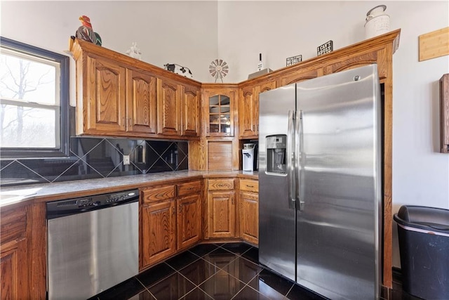 kitchen featuring tasteful backsplash, glass insert cabinets, brown cabinetry, stainless steel appliances, and dark tile patterned flooring