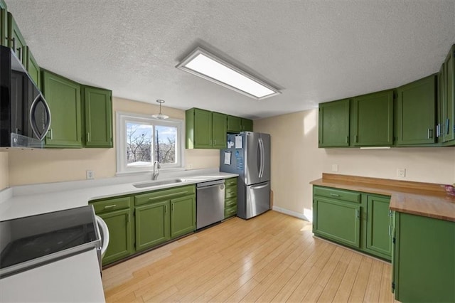 kitchen with green cabinetry, a sink, stainless steel appliances, a textured ceiling, and light wood-type flooring