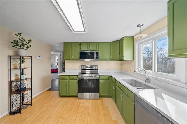 kitchen featuring light wood finished floors, green cabinetry, light countertops, stainless steel appliances, and a sink