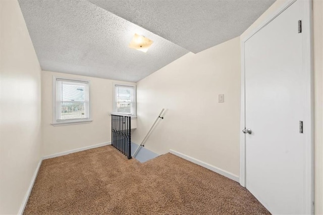 unfurnished bedroom featuring a textured ceiling, lofted ceiling, baseboards, and carpet floors