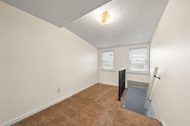 empty room featuring carpet flooring, a textured ceiling, baseboards, and vaulted ceiling