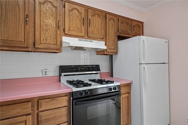 kitchen featuring under cabinet range hood, decorative backsplash, brown cabinets, freestanding refrigerator, and gas stove