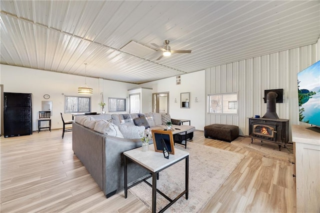 living room featuring ceiling fan, a wood stove, and light wood-style floors