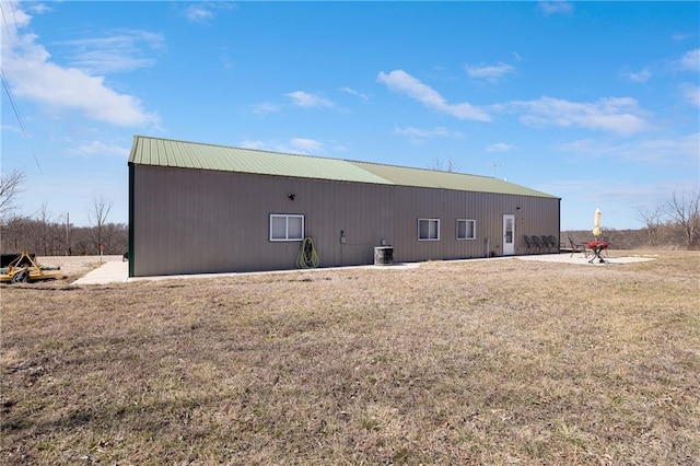 back of house featuring an outbuilding, a lawn, central AC, an outdoor structure, and metal roof