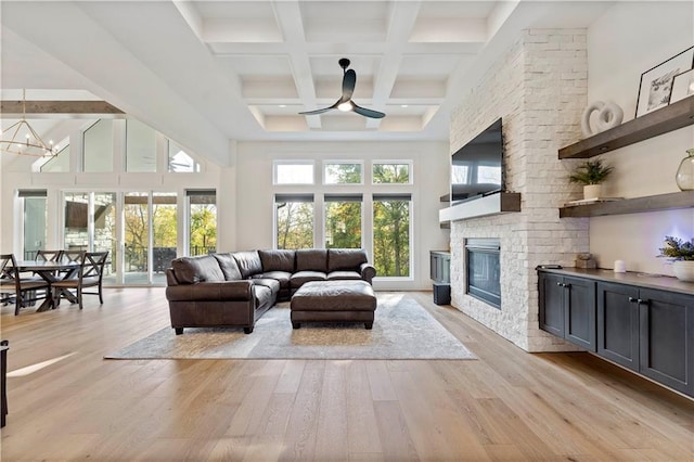 living room featuring a high ceiling, a fireplace, light wood-style floors, beamed ceiling, and ceiling fan with notable chandelier