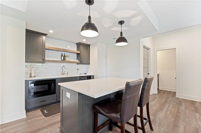 kitchen with black microwave, light countertops, light wood-type flooring, decorative backsplash, and a sink