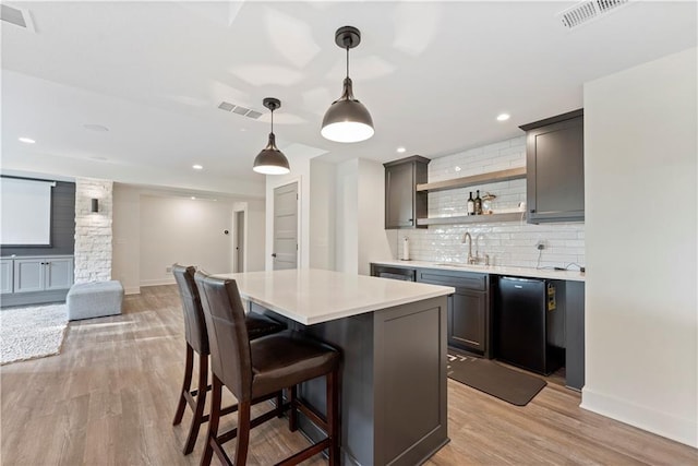 kitchen featuring visible vents, light wood-style flooring, a sink, backsplash, and light countertops