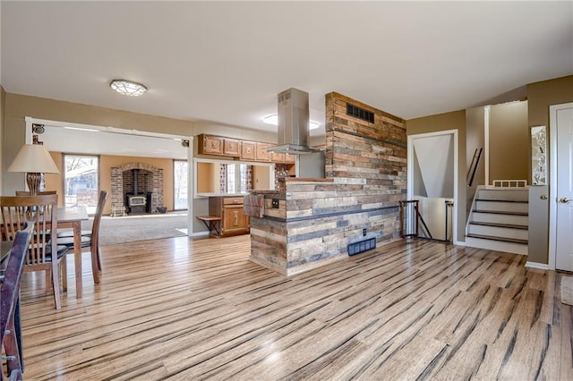 living room with visible vents, stairs, light wood-style floors, and a wood stove