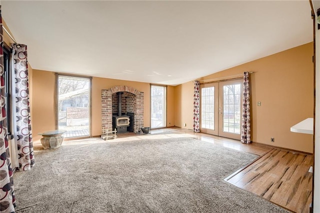 unfurnished living room featuring wood finished floors, french doors, carpet, lofted ceiling, and a wood stove