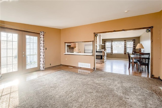 unfurnished living room featuring wood finished floors, visible vents, carpet floors, baseboards, and french doors