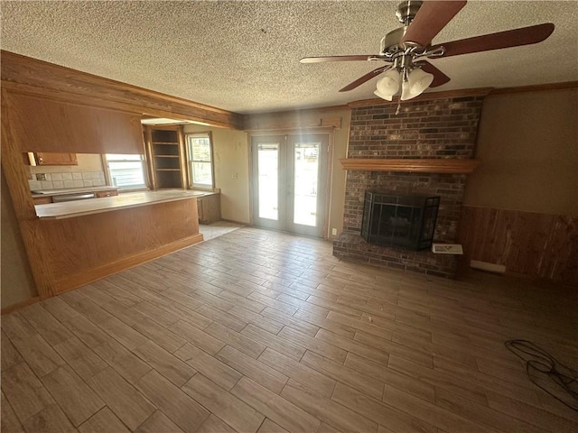 unfurnished living room featuring wooden walls, a brick fireplace, wood finished floors, a textured ceiling, and a ceiling fan