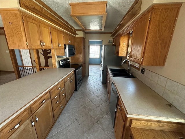 kitchen featuring light countertops, appliances with stainless steel finishes, brown cabinetry, a textured ceiling, and a sink