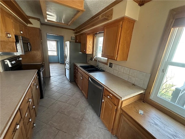 kitchen featuring brown cabinets, a sink, backsplash, stainless steel appliances, and light countertops