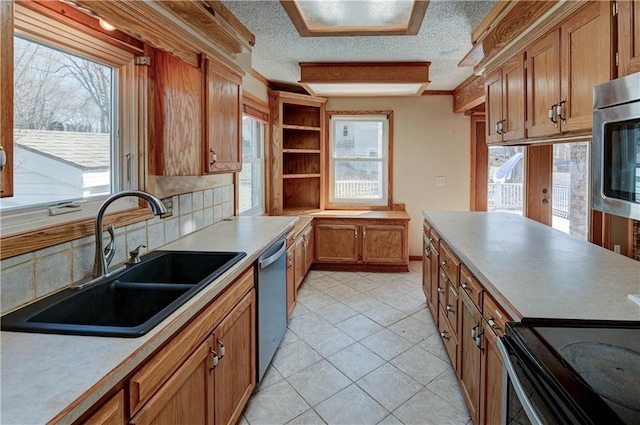 kitchen featuring brown cabinetry, stainless steel appliances, decorative backsplash, a sink, and a textured ceiling