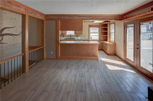 kitchen with light wood-style flooring, a sink, french doors, a peninsula, and light countertops