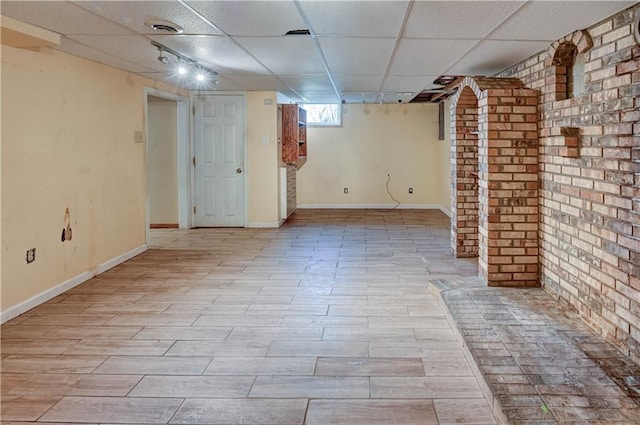 basement featuring wood finished floors, visible vents, baseboards, brick wall, and a paneled ceiling