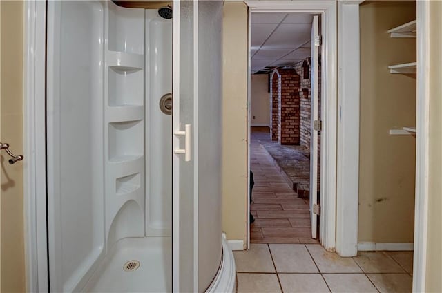 full bath with tile patterned floors, a paneled ceiling, brick wall, and a shower stall