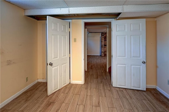 interior space with light wood-style flooring, a paneled ceiling, and baseboards