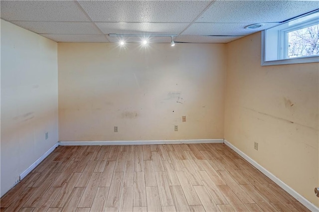 basement featuring light wood-type flooring, a paneled ceiling, baseboards, and rail lighting