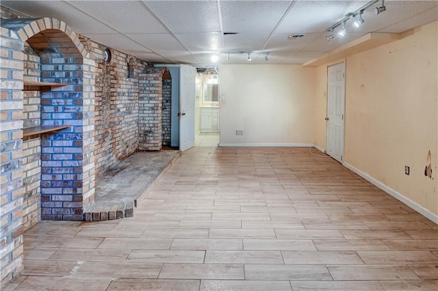 finished basement featuring baseboards, brick wall, wood finished floors, and track lighting