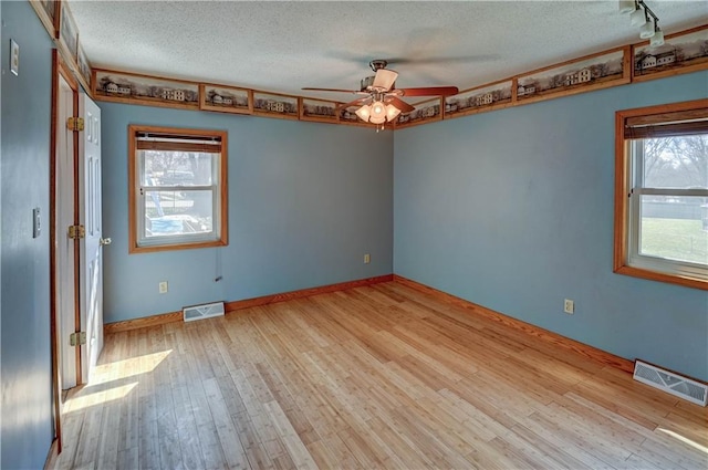 empty room with visible vents, a textured ceiling, a ceiling fan, and wood-type flooring