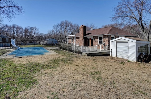 view of pool with a water slide, fence, a yard, an outbuilding, and a storage unit