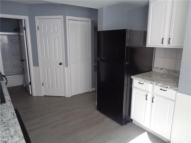 kitchen with tasteful backsplash, light wood finished floors, light stone countertops, freestanding refrigerator, and white cabinets