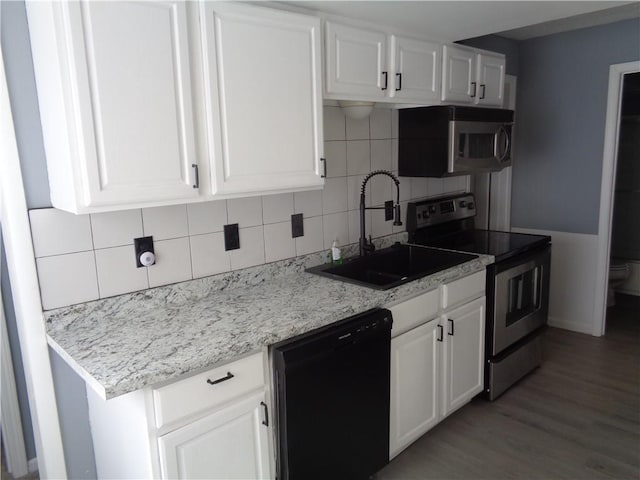 kitchen with wood finished floors, a sink, stainless steel appliances, white cabinetry, and tasteful backsplash