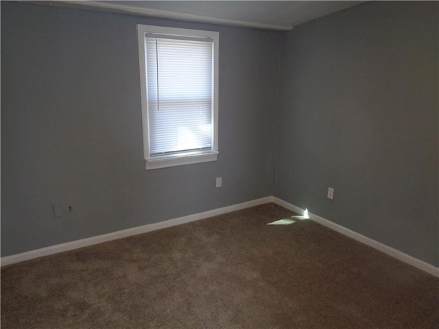 spare room with baseboards and dark carpet