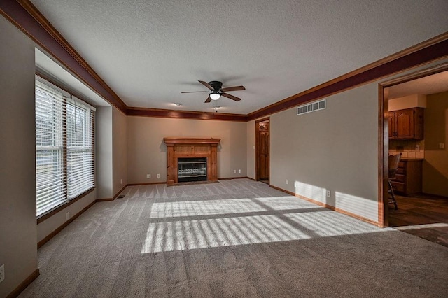 unfurnished living room with visible vents, light carpet, a fireplace with flush hearth, ornamental molding, and a textured ceiling