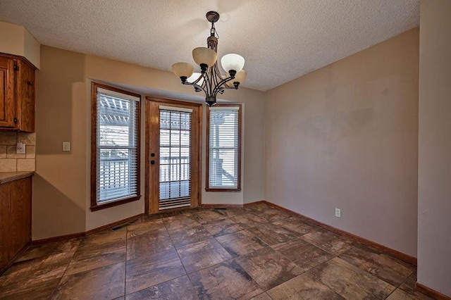 unfurnished dining area featuring visible vents, a textured ceiling, baseboards, and an inviting chandelier