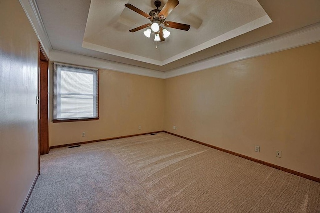 carpeted empty room with visible vents, a raised ceiling, ornamental molding, a ceiling fan, and baseboards