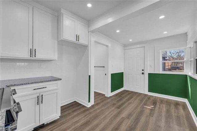 kitchen with light stone countertops, baseboards, dark wood-type flooring, white cabinets, and backsplash