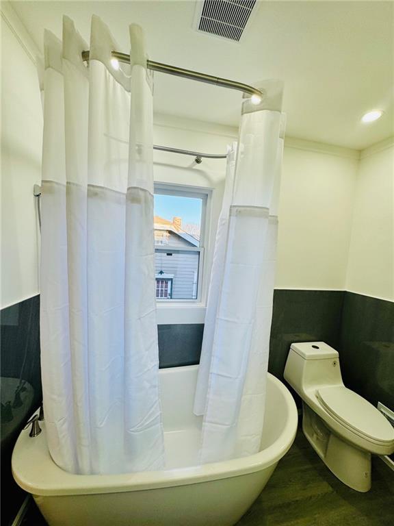 1901 E 79th St, Kansas City, MO 64132 - full bath featuring wood finished floors, visible vents, shower / bath combo, wainscoting, and toilet