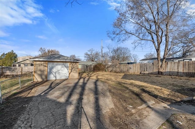 view of yard featuring a detached garage, an outbuilding, fence, and driveway