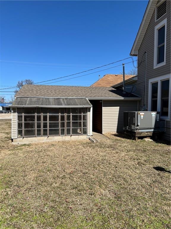 exterior space with a yard, a sunroom, and roof with shingles