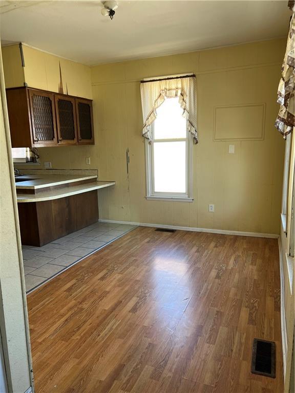 kitchen featuring visible vents, light wood-style flooring, light countertops, glass insert cabinets, and baseboards