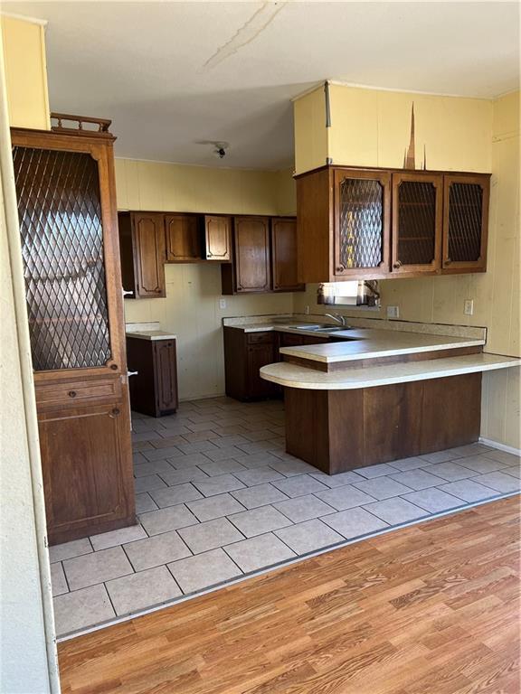 kitchen with a sink, light wood-style floors, a peninsula, dark brown cabinetry, and light countertops