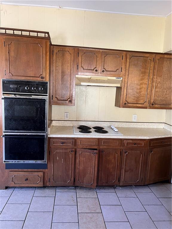 kitchen with light tile patterned floors, light countertops, under cabinet range hood, dobule oven black, and white electric cooktop