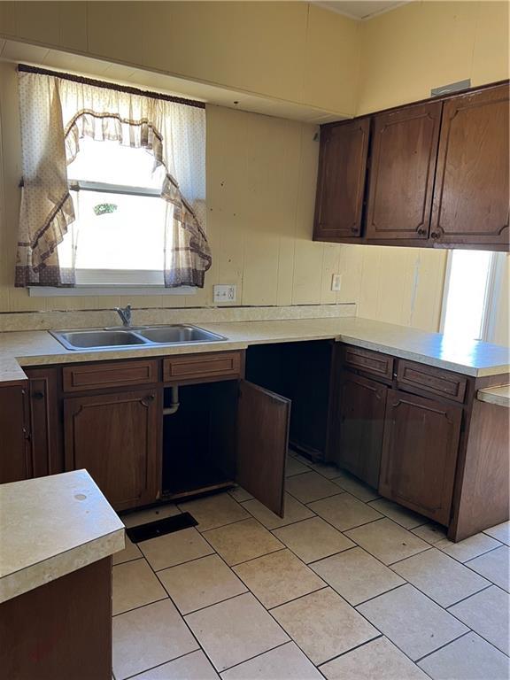 kitchen with a peninsula, light tile patterned flooring, a sink, light countertops, and dark brown cabinets